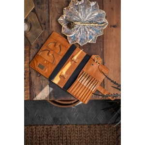 Een opengeklapte bruine opbergetui met vakken voor haaknaalden, kabels en andere accessoires, liggend op een rustieke houten tafel.