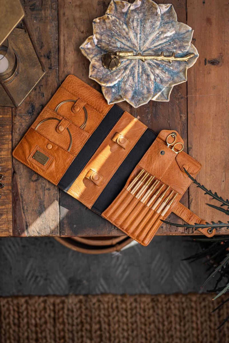 Muud Carita | Het Wolhuis Een opengeklapte bruine opbergetui met vakken voor haaknaalden, kabels en andere accessoires, liggend op een rustieke houten tafel.